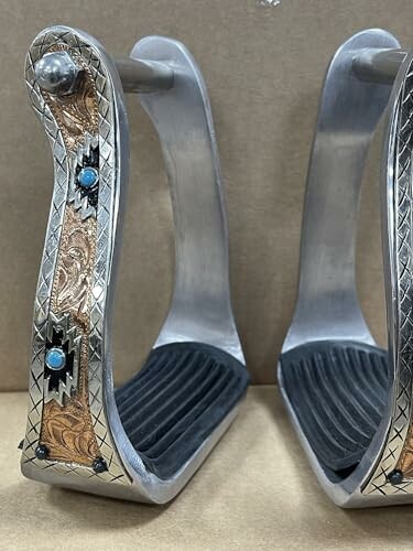 Pair of decorative metal horse stirrups with engraved designs and turquoise accents.